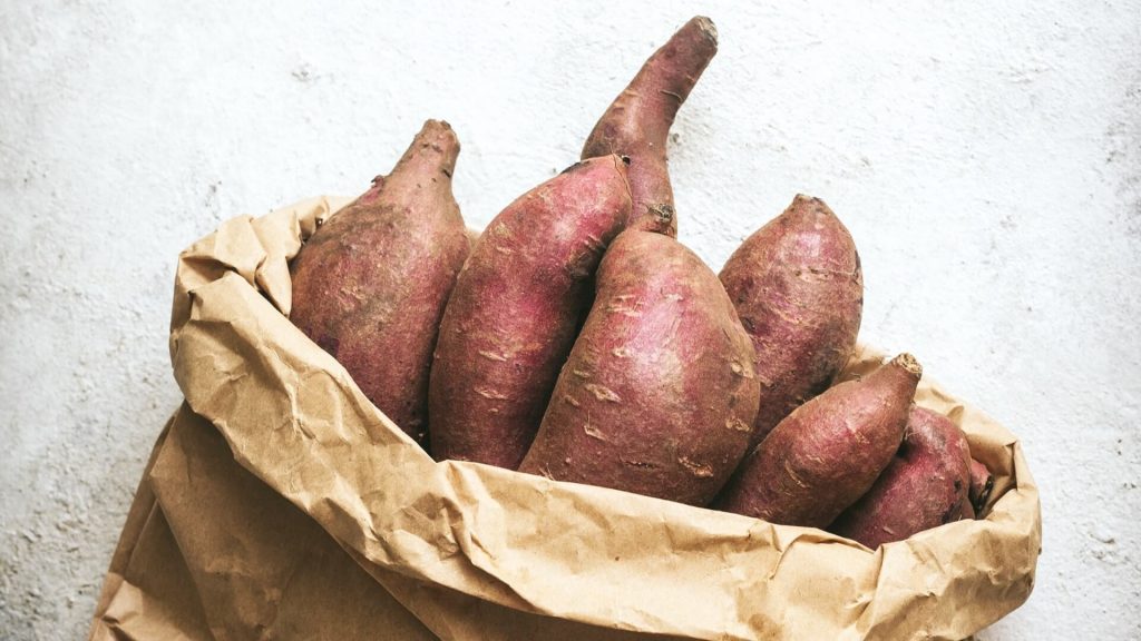 Paper bag filled with sweet potatoes.